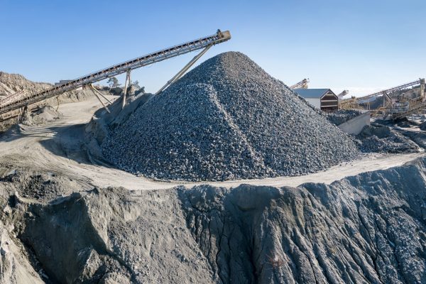 Huge pile of gravel and machinery at stone crushing and screening plant, over blue sky